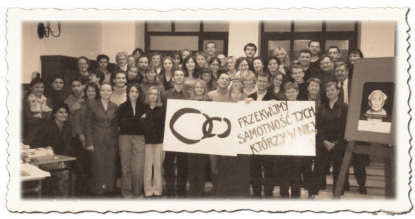 Grupa ludzi trzyma znak z napisem: Przerwijmy samotność tych, którzy w niej... Ostatnie słowo jest niewidoczne przez flesz